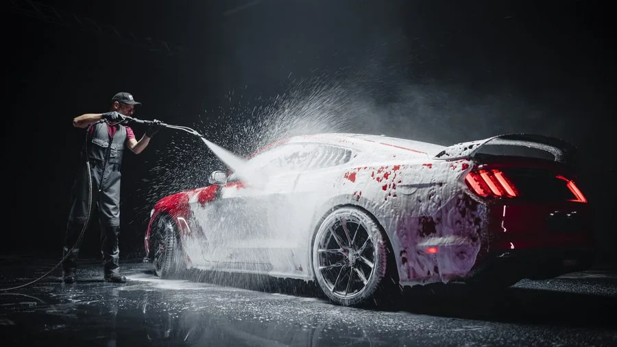 Technician hand-washing and pressure-washing a vehicle